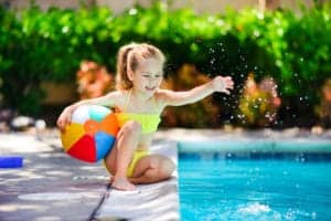 Little girl with a beach ball next to a swimming pool.
